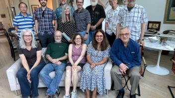 Group of 15 adults in a living room, posing together on and around a couch for a reunion-style photo.