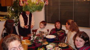 Group gathered around a dinner table with holiday food and decorations under a hanging light.
