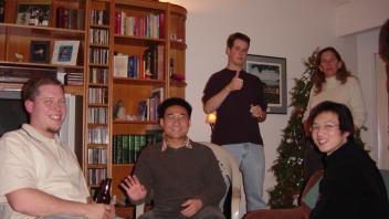 Group of five people standing and sitting in a living room near a decorated Christmas tree.