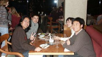 Four people sitting at a booth table in a restaurant, smiling and making peace signs.