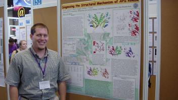 Man standing next to a scientific research poster titled “Diagnosing the Structural Mechanism of APS kinase” at a conference.