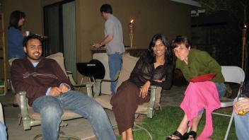 Three people relaxing on lawn chairs in a backyard at night, with tiki torches and a barbecue in the background.