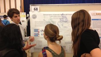 Student explains a research poster on Entamoeba histolytica APS Kinase to a group of attendees at a poster session.