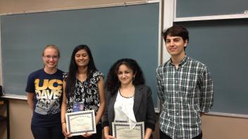 Four students stand in front of a chalkboard, two holding certificates from the University of California, Davis.