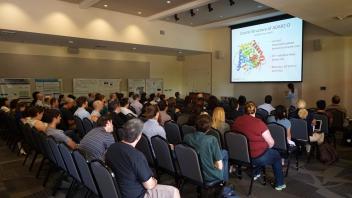 Large audience seated and watching a scientific presentation about protein structure.