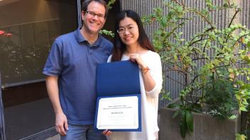 Man and woman posing outside, holding a certificate for academic recognition.