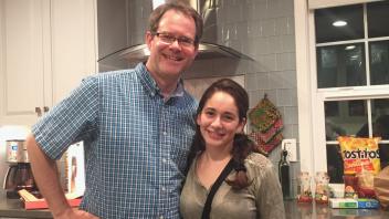 Two people posing and smiling in a modern kitchen with snacks on the counter.