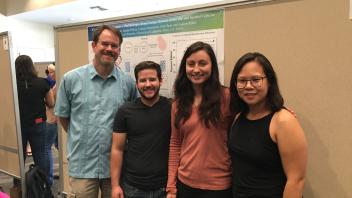 Four people posing in front of a scientific research poster presentation.