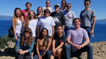Large group of people posing outdoors on a mountain with a lake in the background.