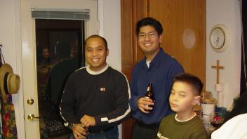 Two men holding drinks and a young boy gather in a kitchen near a back door.